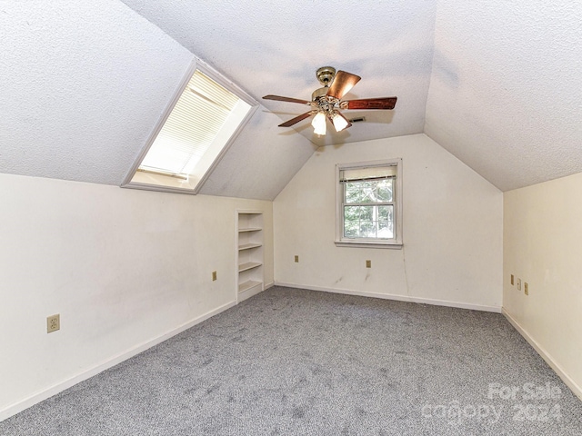 additional living space with ceiling fan, light colored carpet, a textured ceiling, and lofted ceiling with skylight