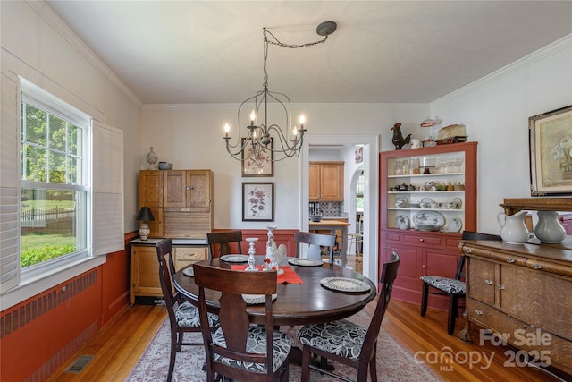 dining area with radiator heating unit, crown molding, hardwood / wood-style floors, and an inviting chandelier