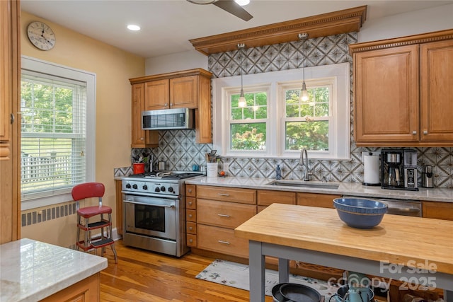 kitchen featuring pendant lighting, radiator heating unit, sink, stainless steel appliances, and light wood-type flooring