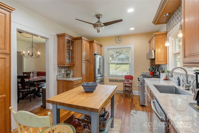 kitchen featuring sink, radiator, appliances with stainless steel finishes, a wealth of natural light, and light stone countertops