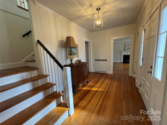 foyer with ornamental molding, wood-type flooring, radiator, and a notable chandelier