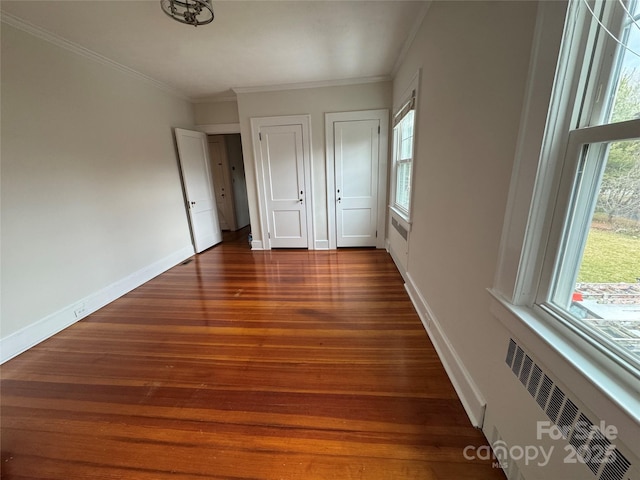 unfurnished bedroom with ornamental molding, dark hardwood / wood-style flooring, radiator, and two closets