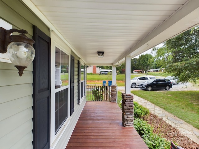 wooden terrace featuring a lawn and a porch