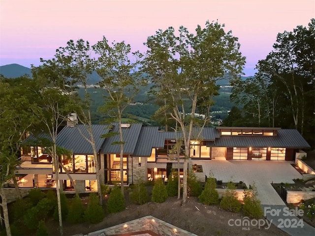 back of property at dusk featuring stone siding, metal roof, and a standing seam roof