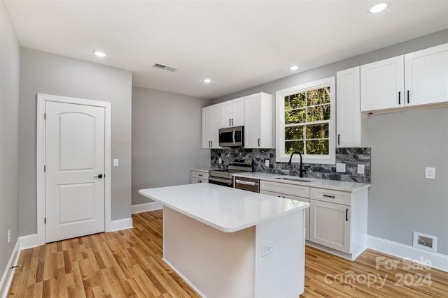 kitchen with white cabinets, a center island, appliances with stainless steel finishes, light hardwood / wood-style floors, and sink