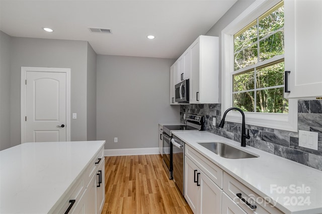 kitchen with light hardwood / wood-style flooring, tasteful backsplash, stainless steel appliances, sink, and white cabinetry