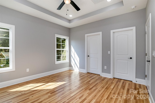 unfurnished bedroom with light hardwood / wood-style flooring, a raised ceiling, and multiple windows