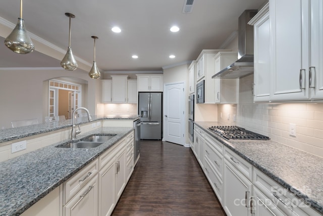 kitchen with appliances with stainless steel finishes, wall chimney exhaust hood, sink, decorative light fixtures, and white cabinets