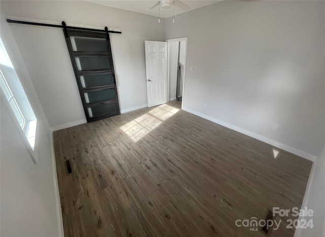 unfurnished room featuring a barn door, dark hardwood / wood-style floors, and ceiling fan