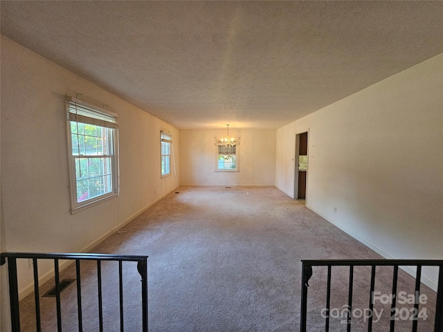 carpeted spare room with a textured ceiling and a chandelier