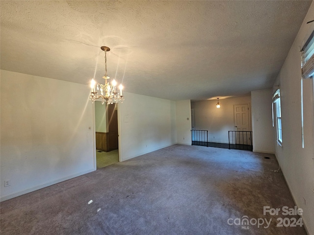 carpeted empty room featuring a textured ceiling and a notable chandelier