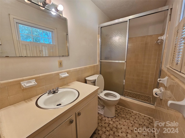 bathroom with toilet, a shower with door, vanity, backsplash, and tile walls