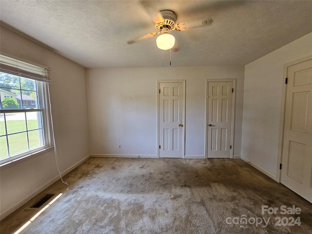 unfurnished bedroom with a textured ceiling, two closets, ceiling fan, and carpet flooring