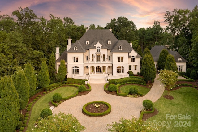 view of front of house featuring stucco siding, a balcony, curved driveway, and a front yard