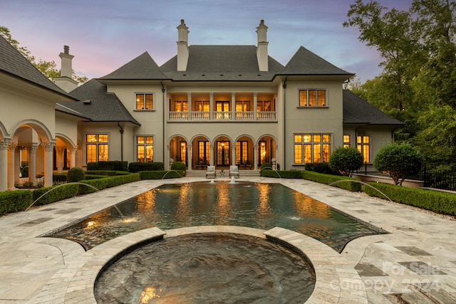 back house at dusk with french doors, a patio area, a swimming pool with hot tub, and pool water feature