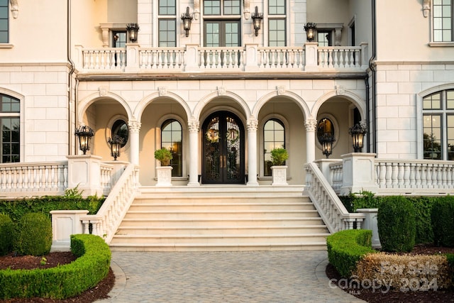 view of exterior entry featuring stone siding, covered porch, french doors, and a balcony