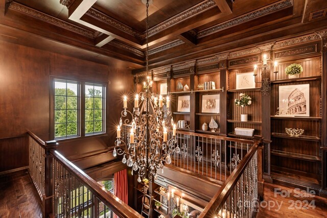 wine area with coffered ceiling, a notable chandelier, wood finished floors, and ornamental molding