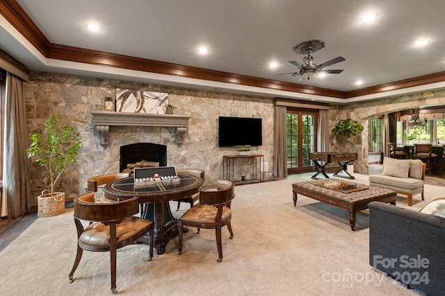 carpeted dining area featuring a tray ceiling, ceiling fan, crown molding, and a stone fireplace