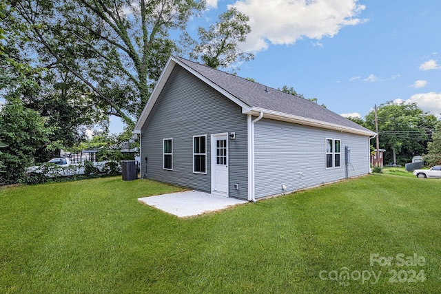 rear view of house with a patio area, a shingled roof, central AC, and a yard