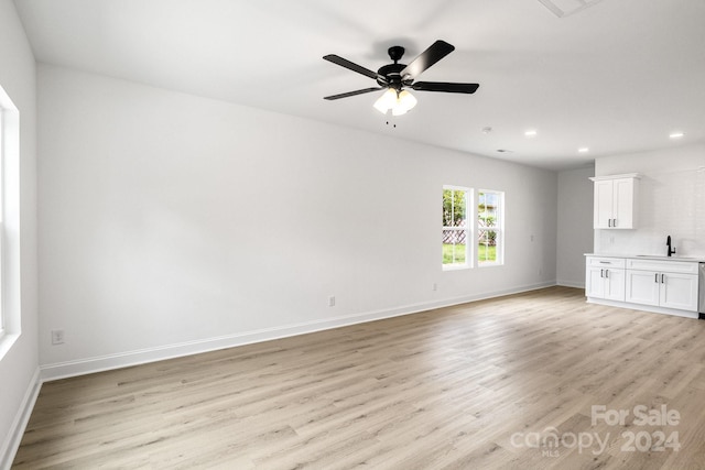 unfurnished living room featuring a ceiling fan, baseboards, a sink, and light wood finished floors