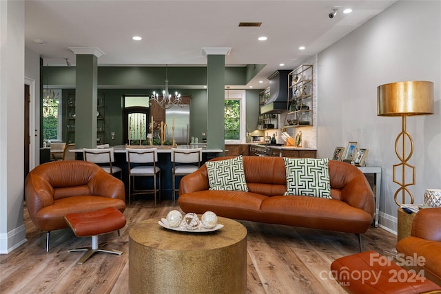 living room with wood-type flooring, ornate columns, and an inviting chandelier