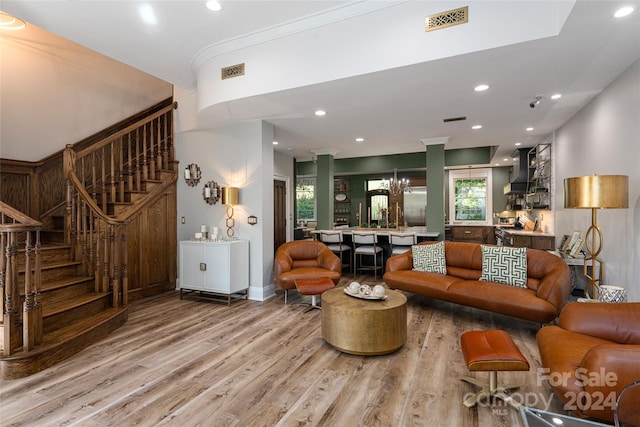 living room featuring crown molding, light hardwood / wood-style flooring, a chandelier, and decorative columns