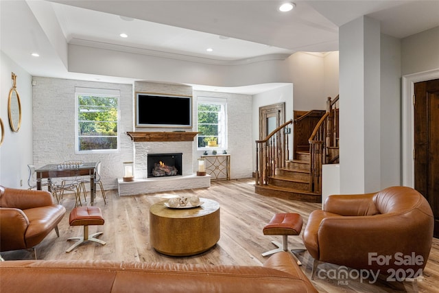 living room featuring a healthy amount of sunlight, ornamental molding, a stone fireplace, and light wood-type flooring