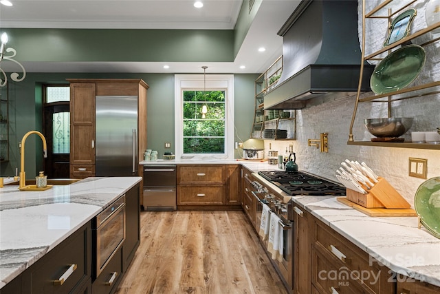 kitchen with custom exhaust hood, crown molding, light hardwood / wood-style flooring, light stone counters, and premium appliances