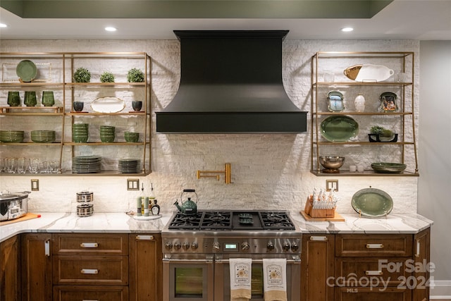 interior space featuring custom exhaust hood, light stone countertops, backsplash, and double oven range