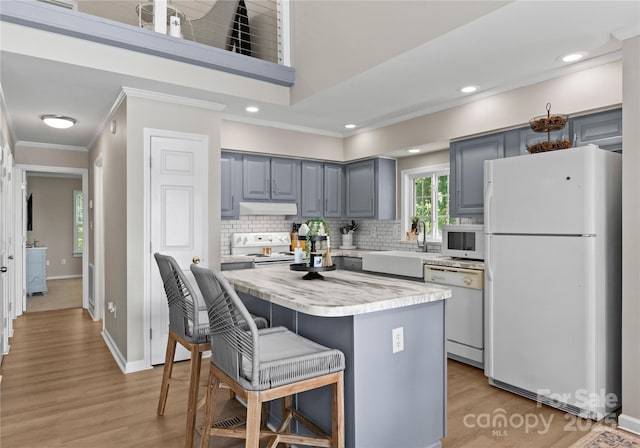 kitchen with white appliances, sink, light hardwood / wood-style flooring, a kitchen island, and a breakfast bar area