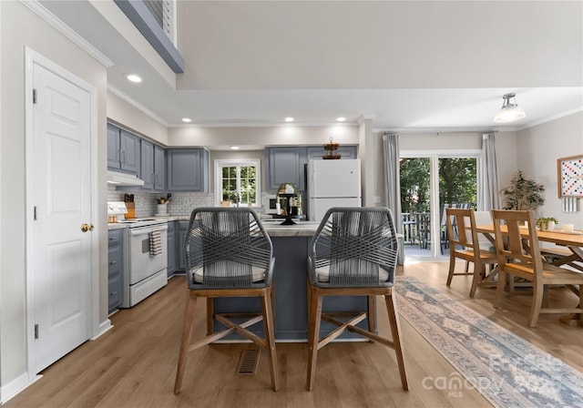 kitchen featuring gray cabinetry, backsplash, light wood-type flooring, white appliances, and ornamental molding