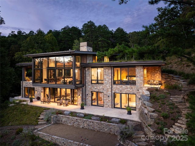 back house at dusk featuring a sunroom and a patio