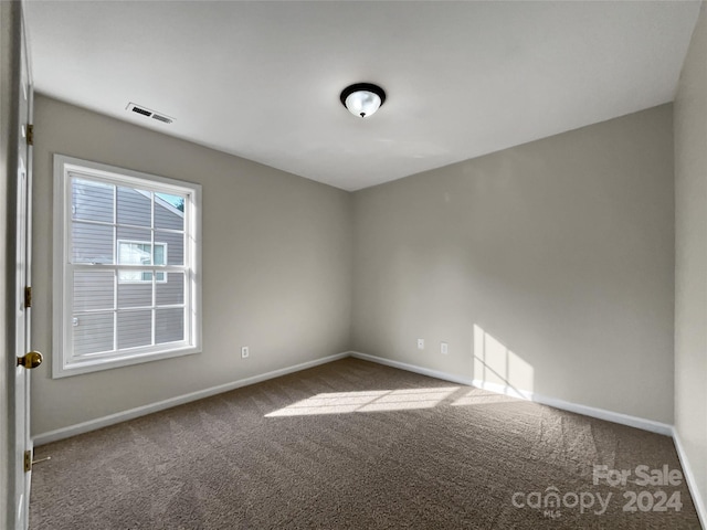 empty room with carpet, visible vents, and baseboards