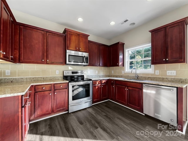 kitchen with reddish brown cabinets, stainless steel appliances, a sink, and light stone countertops