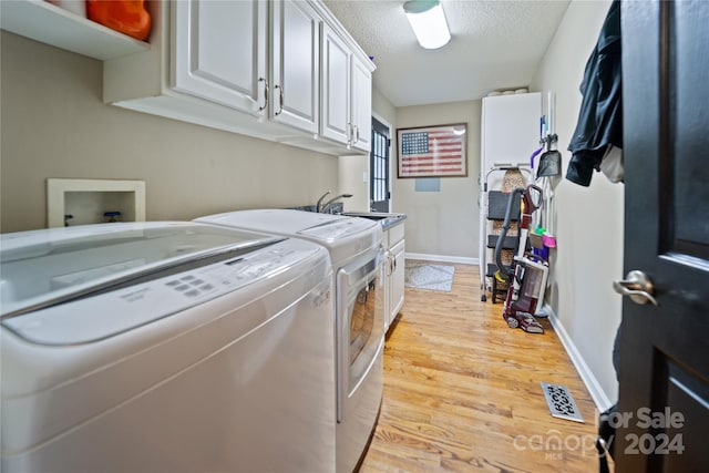10235 Mount Holly Rd, Charlotte, NC 28214 - clothes washing area with cabinets, a textured ceiling, sink, light hardwood / wood-style flooring, and washing machine and dryer
