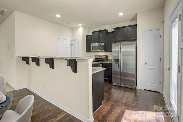 kitchen featuring a breakfast bar, stainless steel appliances, light stone countertops, and dark hardwood / wood-style flooring