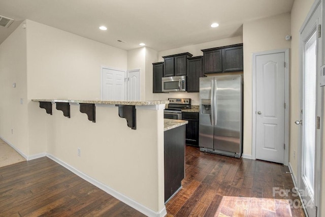 kitchen featuring appliances with stainless steel finishes, light stone countertops, dark hardwood / wood-style flooring, kitchen peninsula, and a kitchen breakfast bar