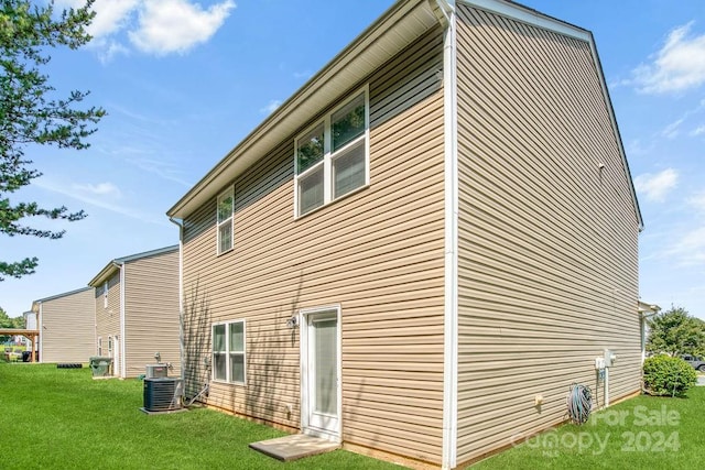 back of house with central AC unit and a yard