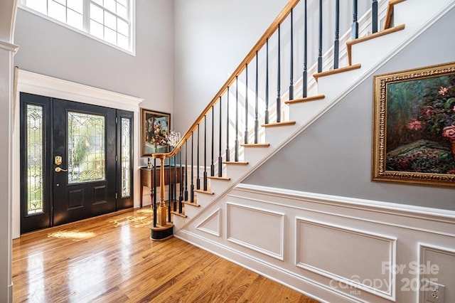 foyer entrance featuring a wainscoted wall, a high ceiling, stairway, and wood finished floors