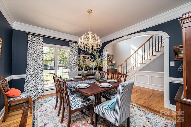 dining room featuring arched walkways, stairway, ornamental molding, wood finished floors, and an inviting chandelier