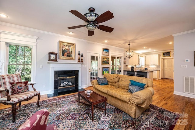 living room featuring crown molding, visible vents, light wood-style floors, a tile fireplace, and baseboards