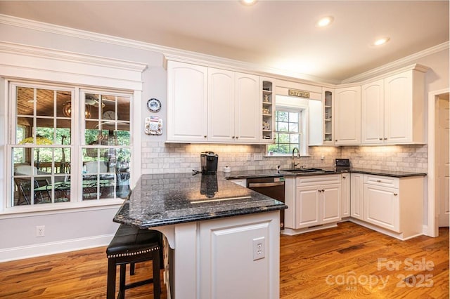 kitchen featuring white cabinets, light wood-style flooring, a kitchen breakfast bar, a peninsula, and a sink