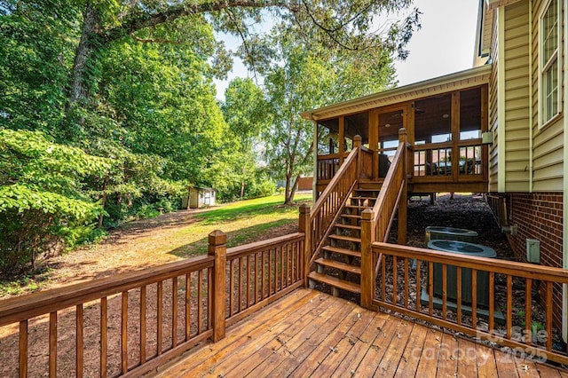 deck featuring central AC unit, an outdoor structure, stairs, a lawn, and a shed