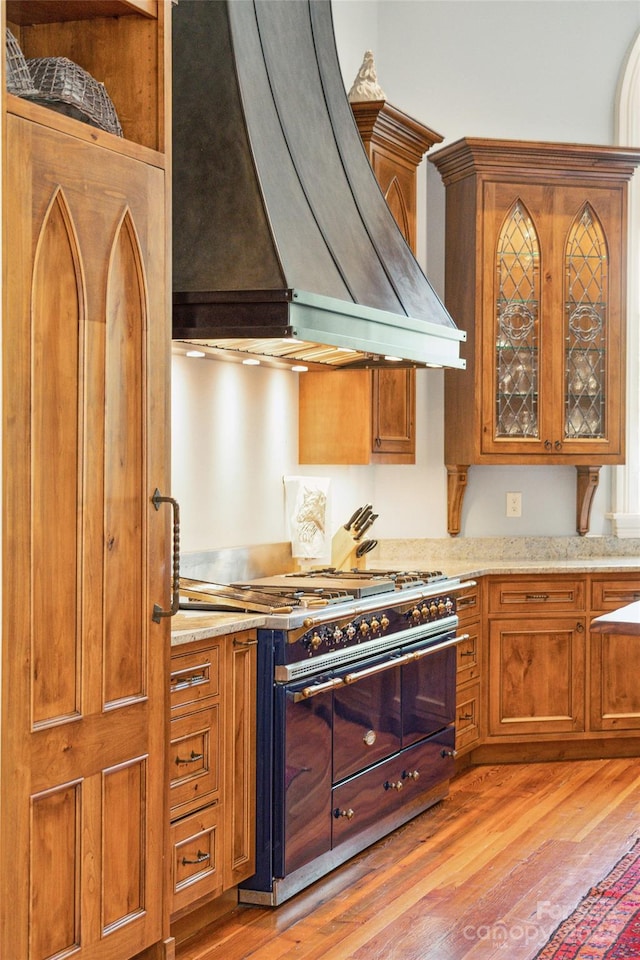 kitchen featuring light stone countertops, custom exhaust hood, high end range, and light hardwood / wood-style floors