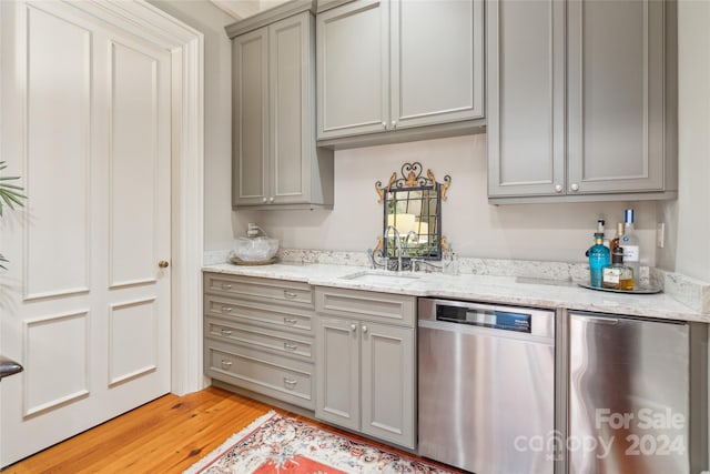 kitchen with light hardwood / wood-style flooring, stainless steel appliances, light stone counters, sink, and gray cabinetry