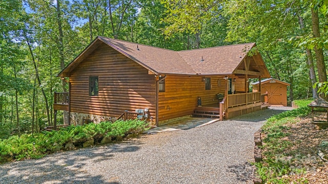 exterior space featuring roof with shingles, a deck, an outbuilding, stone siding, and a storage unit