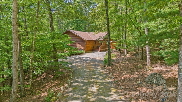 view of front of home featuring faux log siding, a wooded view, and gravel driveway