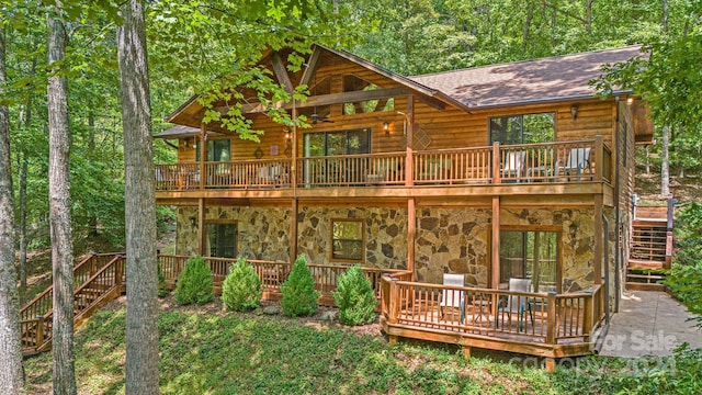 back of house with a wooden deck, stone siding, roof with shingles, and stairs