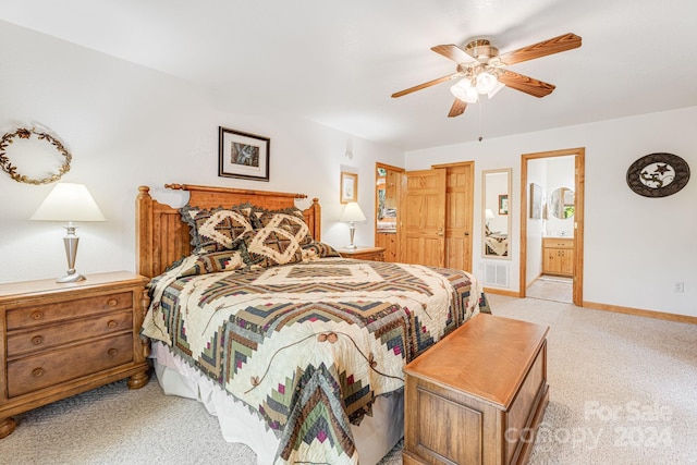 bedroom featuring a ceiling fan, light colored carpet, baseboards, and ensuite bathroom