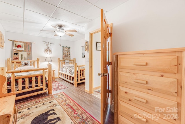 bedroom with ceiling fan, a drop ceiling, baseboards, and wood finished floors